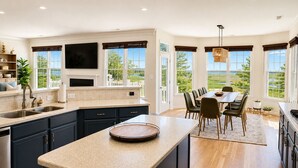 A modern kitchen with a large island, dining area with a view, and a flat-screen TV mounted above the island. - Stunning Bayside View Retreat; Resort, Pools & Gym (Berlin)