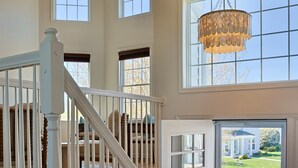 A spacious interior with a staircase, large windows, and a chandelier. - Stunning Bayside View Retreat; Resort, Pools & Gym (Berlin)