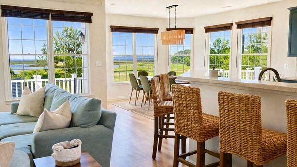 A spacious living area with a sofa, wicker chairs, a dining table, and large windows offering a view of the outdoors. - Stunning Bayside View Retreat; Resort, Pools & Gym (Berlin)
