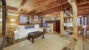 L’intérieur d’un chalet confortable, avec une décoration chaleureuse : un canapé blanc, une table basse en bois et une bibliothèque.