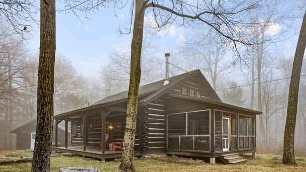 Une cabane rustique dotée d’une véranda, de grandes fenêtres et d’une cheminée.