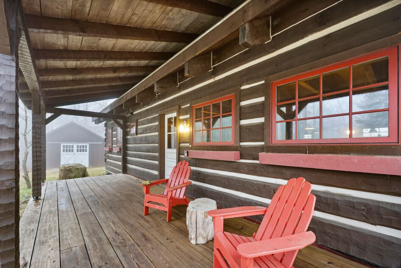 Une cabane en rondins avec un porche, deux fauteuils Adirondack rouges et une petite table ronde.