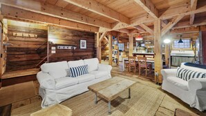 L’intérieur chaleureux d’un chalet avec un plafond en bois, un canapé blanc, un banc en bois et un coin repas comprenant une table et des chaises.