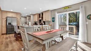 Una cocina moderna con armarios de madera, un refrigerador de acero inoxidable y un comedor con mesa y sillas de madera.