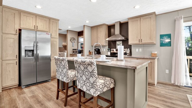Una cocina moderna con armarios de madera, un refrigerador de acero inoxidable y una barra con taburetes estampados.