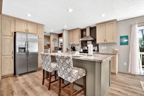 Una cucina moderna con mobili in legno, un frigorifero in acciaio inossidabile e un angolo bar con sgabelli decorati.