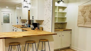 Una cocina con una isla de madera, taburetes de bar, armarios blancos y un mapa del mundo en la pared.