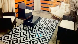 Un rincón al aire libre acogedor con alfombra estampada, una lámpara colgante y una silla de mimbre.