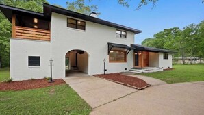 Una casa moderna de dos pisos con fachada blanca, un porche cubierto y un jardín delantero arbolado.