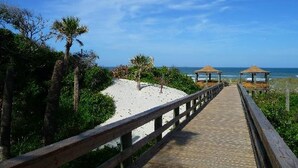 A wooden boardwalk leading to beach huts with a clear view of the ocean. - Tropical Haven 2BR/2BA Near Atlantic Beach (Jacksonville)