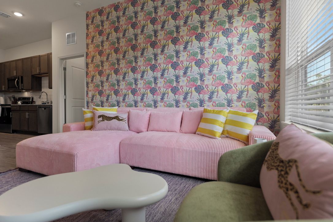 Un salon avec un canapé rose, des coussins à rayures et un mur orné de motifs.