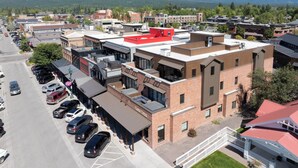 Um edifício de vários andares com telhado vermelho, estacionamento e vista para montanhas ao fundo.