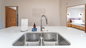 Uma cozinha moderna com uma pia dupla, uma porta de madeira, um objeto decorativo na parede e uma mesinha de cabeceira com um espelho.