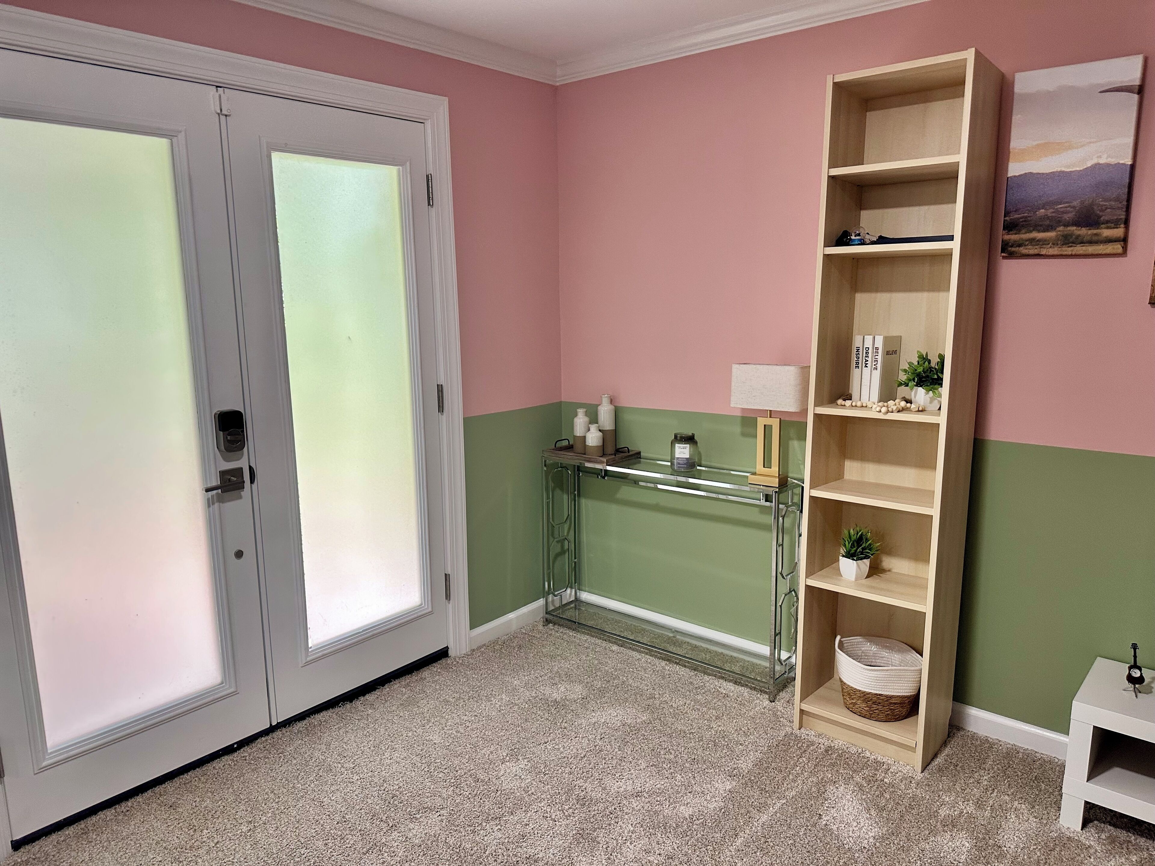 Una habitación con puerta doble, separador de vidrio, estantería de madera y una pequeña mesa blanca.