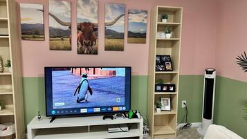 A living room with a flat-screen TV, a bookshelf, and a decorative wall with framed pictures.