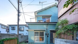 A two-story residential building with a balcony, a small garden area with artificial grass, and a wooden fence. - Showa House – Spacious Retro Stay near Haneda (Ota City)