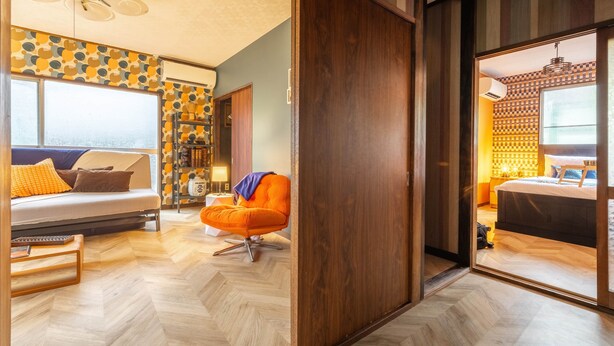 A room with a bed, an orange chair, a wooden floor, and a patterned wall. - Showa House – Spacious Retro Stay near Haneda (Ota City)