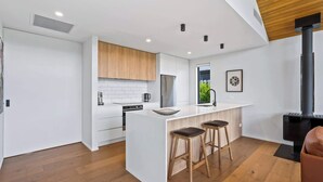 Una cocina moderna con armarios blancos, una isla central con taburetes, una estufa negra y una ventana con vistas a zonas verdes.