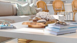 Een gezellige woonkamer met een bank, een bijzettafeltje met boeken en decoratieve objecten, en een uitzicht op de keuken op de achtergrond.