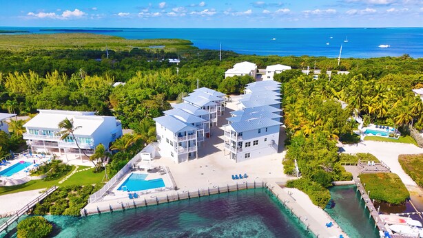 Luchtbeeld van een resort met meerdere gebouwen, een zwembad en helder turquoise water.