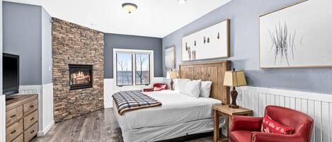 A bedroom with a stone fireplace, a bed, a red armchair, and artwork on the walls.