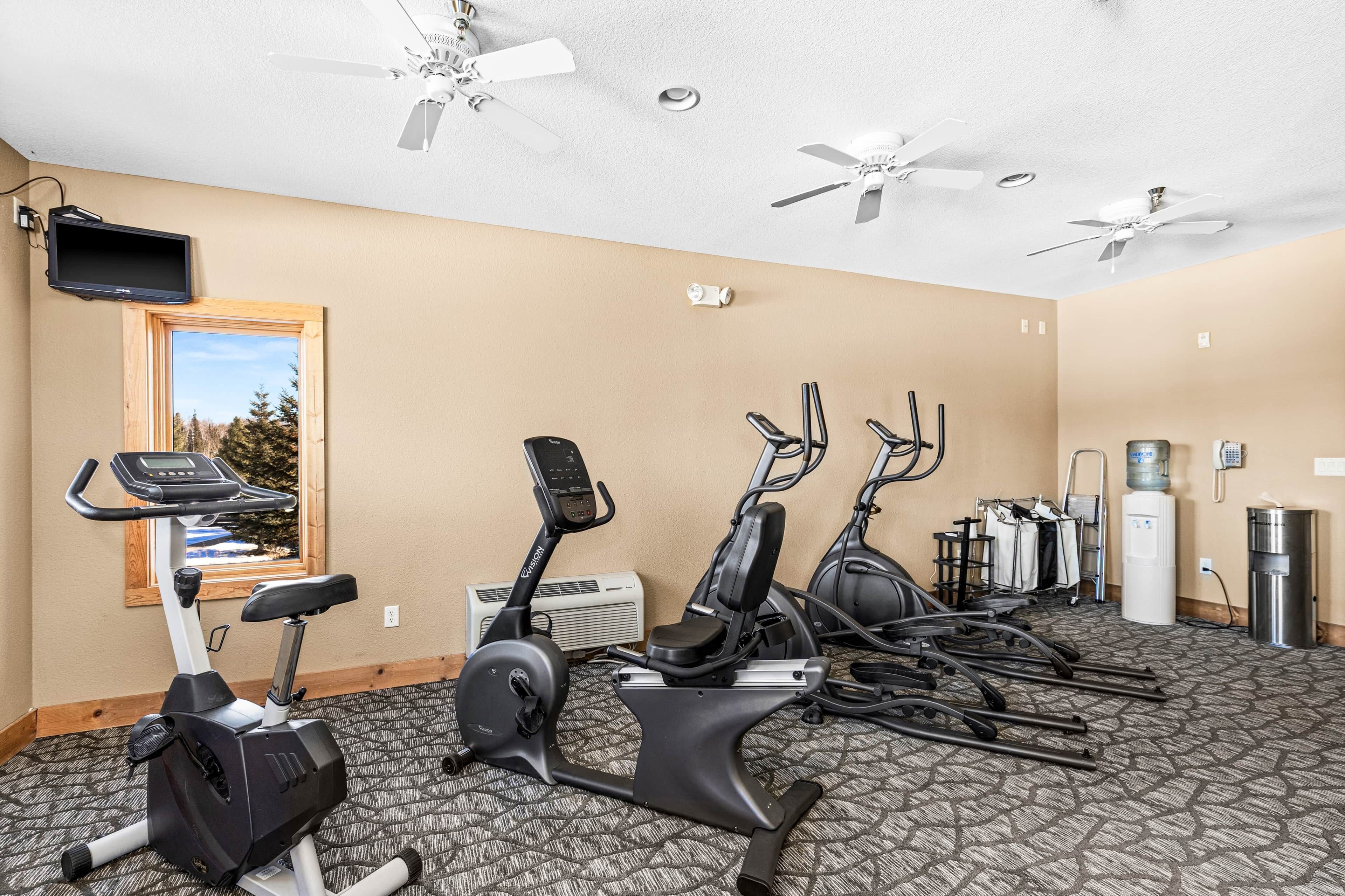 A hotel fitness room with exercise equipment, ceiling fans, and a large window.