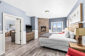 A bedroom with a stone fireplace, a bed, a TV, and a window with a view.