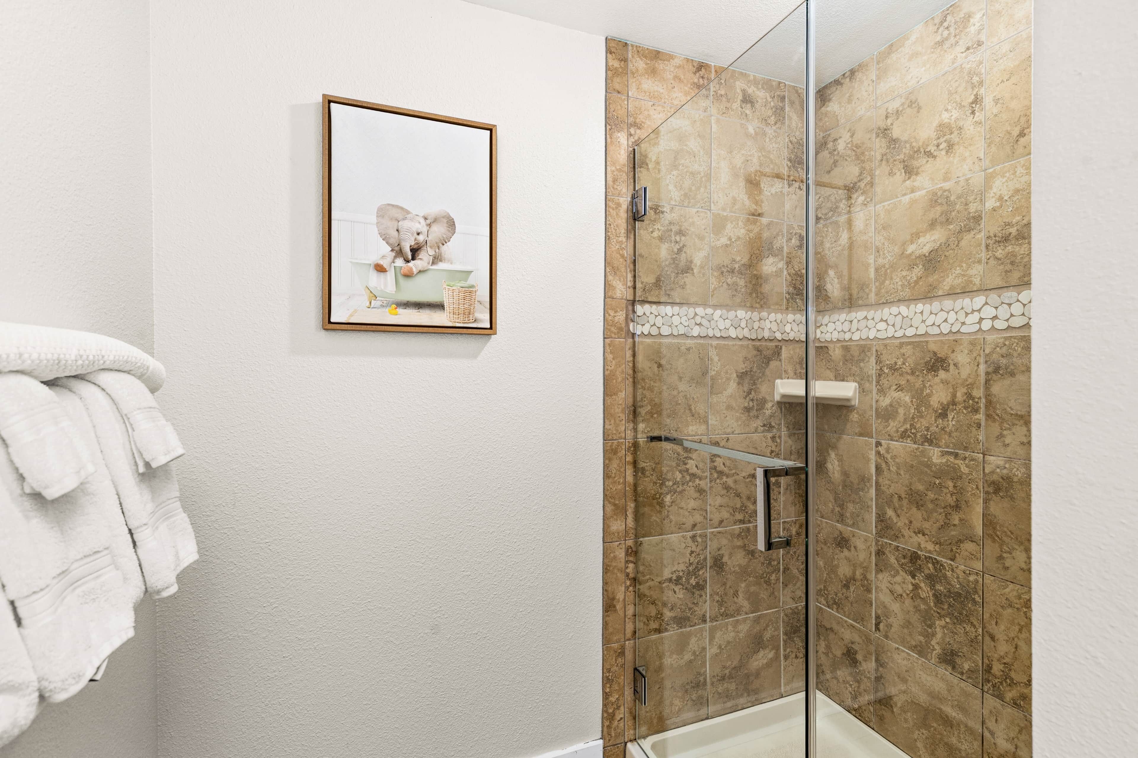 Un baño con cabina de ducha de vidrio, un cuadro enmarcado en la pared y una pila de toallas blancas.