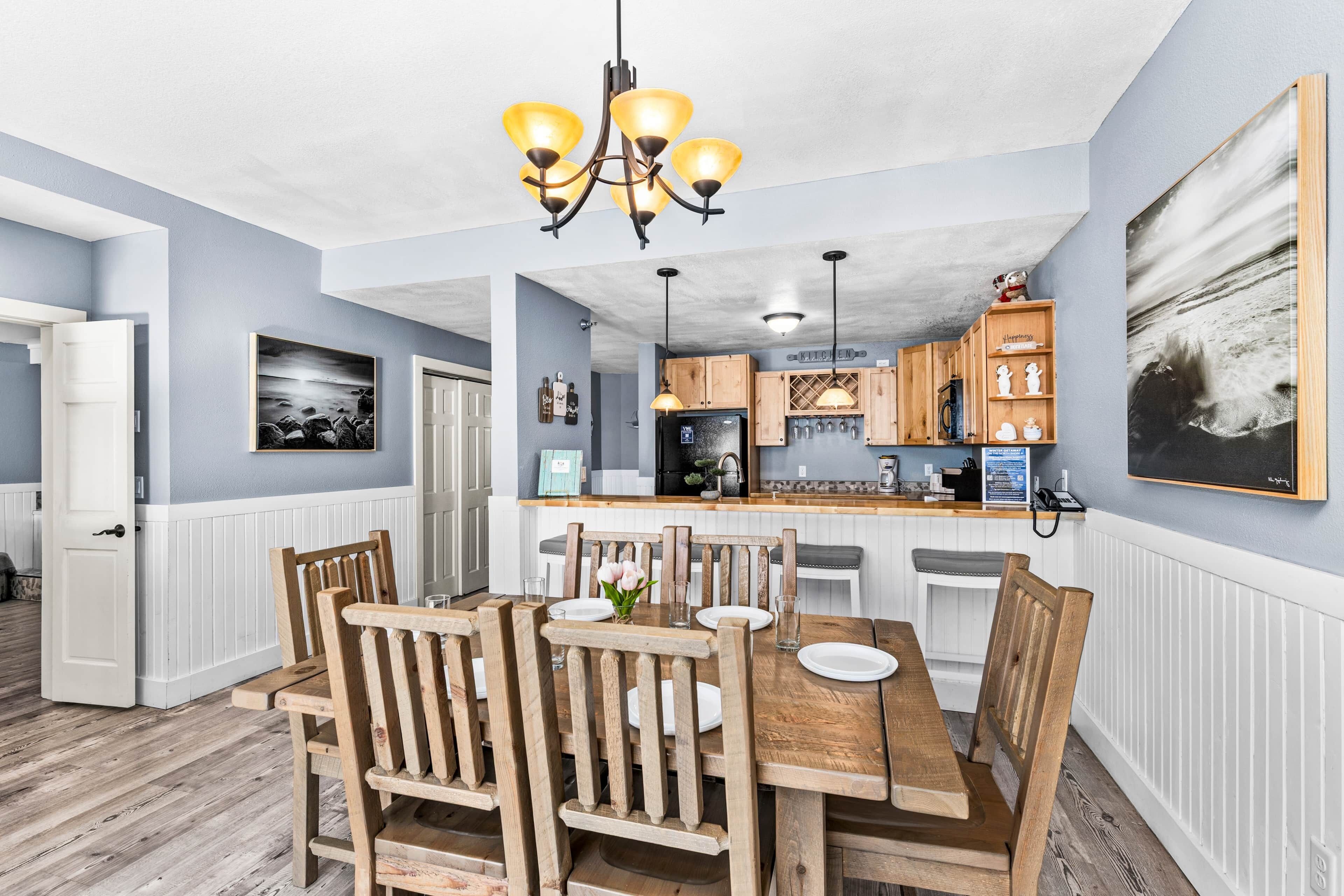 A dining area with wooden chairs and a table, a kitchen with wooden cabinets, and a pendant light.