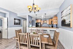 A dining area with wooden chairs and a table, a kitchen with wooden cabinets, and a pendant light. - Whispering Pines Lake Views | 2BR King Suite (Two Harbors)