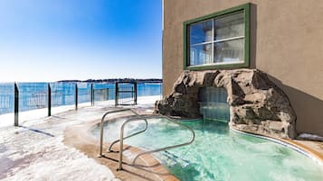 An outdoor pool with a glass barrier, a metal ladder, and a view of the sea.