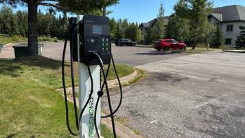A charging station with a digital display, located in a residential area with houses and a red car parked nearby.