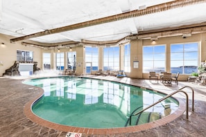 An indoor swimming pool with a stone border, large windows, and a view of the sea. - Whispering Pines Lake Views | 2BR King Suite (Two Harbors)