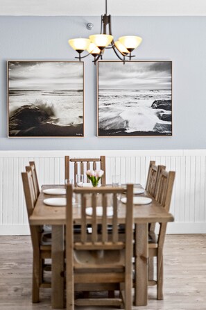 A dining area with a wooden table and chairs, two framed photographs on the wall, and a chandelier. - Whispering Pines Lake Views | 2BR King Suite (Two Harbors)