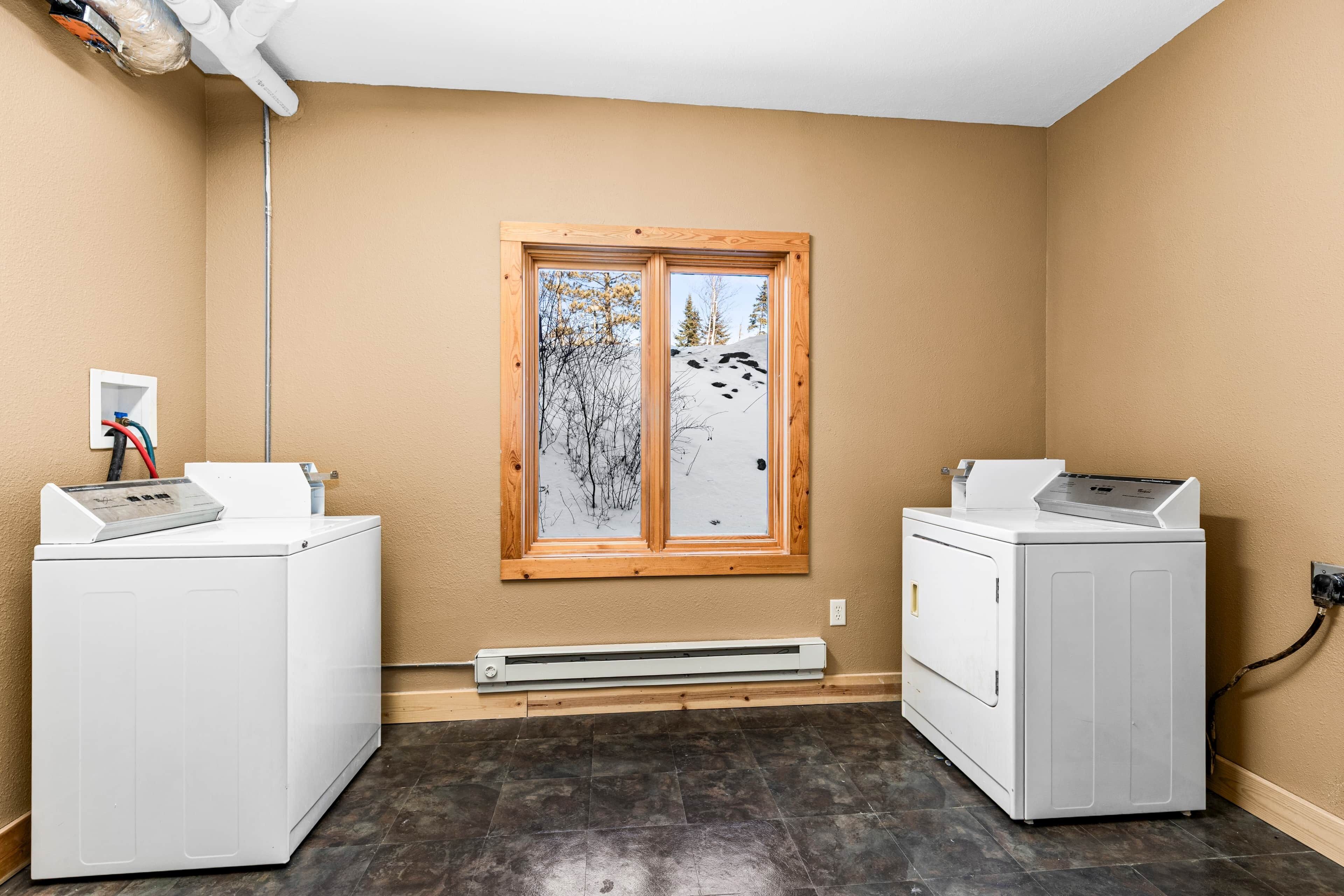 A laundry room with two washing machines, a window with a view of trees and snow, and a wall-mounted heater.