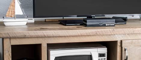A wooden cabinet with a microwave, a small sailboat model, and a Samsung remote control on top.