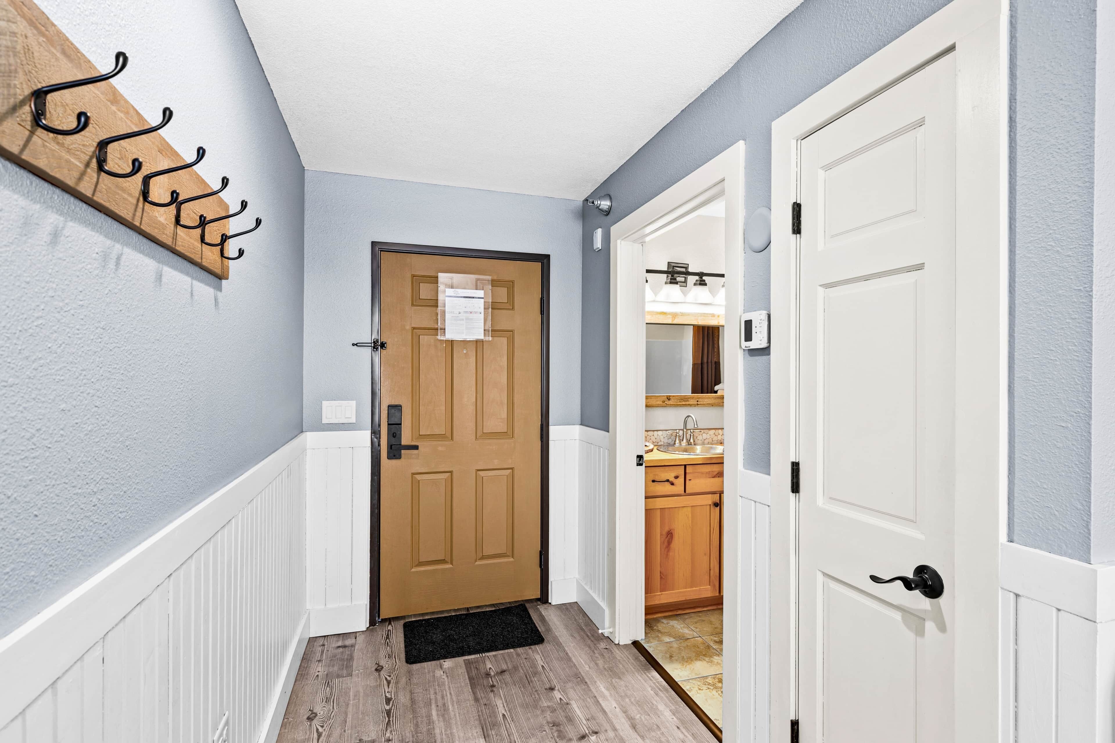 Un pasillo con una puerta de madera, un perchero y una cocina visible a través de una puerta abierta.