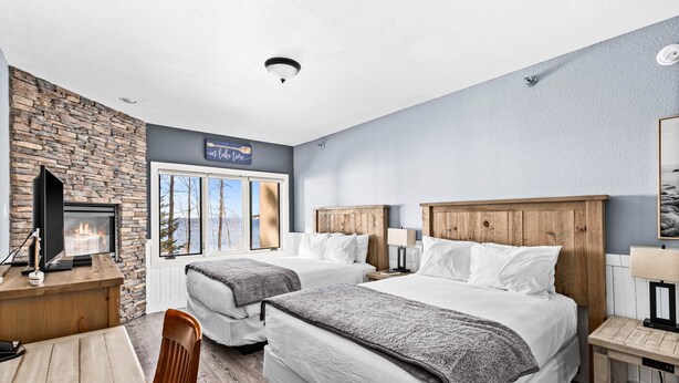 Une chambre d’hôtel avec deux lits, un mur en pierre, une cheminée, un bureau et une fenêtre donnant sur un beau paysage.