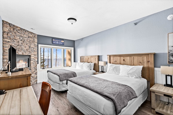A hotel room with two beds, a stone wall, a fireplace, a desk, and a window with a view.