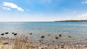 A clear view of a lake with a rocky shoreline and distant trees. - Whispering Pines Lake Views | 2 Queen Bed Studio (Two Harbors)
