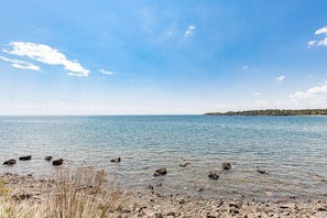 Vista chiara su un lago con una riva rocciosa e alberi in lontananza.