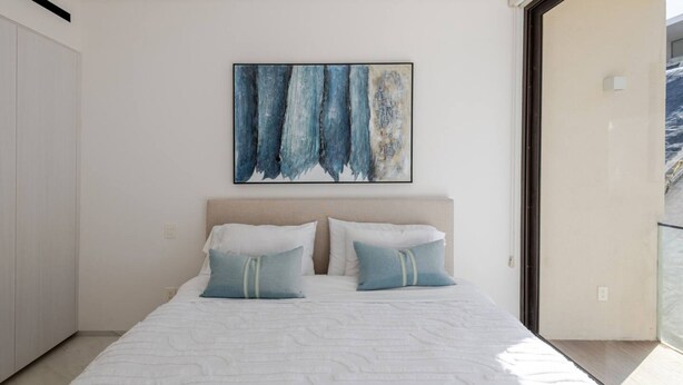 Ein modernes Schlafzimmer mit einem großen Bett, zwei Kissen, einem Kopfteil und einem Gemälde an der Wand.