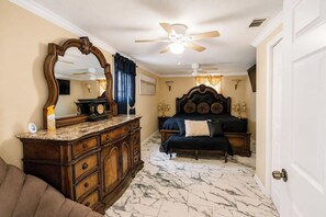 A bedroom with a bed, a dresser, a mirror, a ceiling fan, and a door. - Screened Porch • Gazebo • BBQ • Sleeps 10 (Garden City)