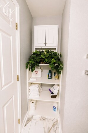 A bathroom with a white cabinet, a shelf with a first aid kit, and a basket with a purple item. - Screened Porch • Gazebo • BBQ • Sleeps 10 (Garden City)