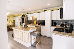 A modern kitchen with white cabinetry, a granite countertop island, and stainless steel appliances. - Screened Porch • Gazebo • BBQ • Sleeps 10 (Garden City)