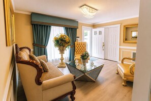 Una sala de estar con un sofá, una mesa de centro de vidrio y un sillón amarillo. Se ve una puerta que conduce a otra habitación y un espejo en la pared.