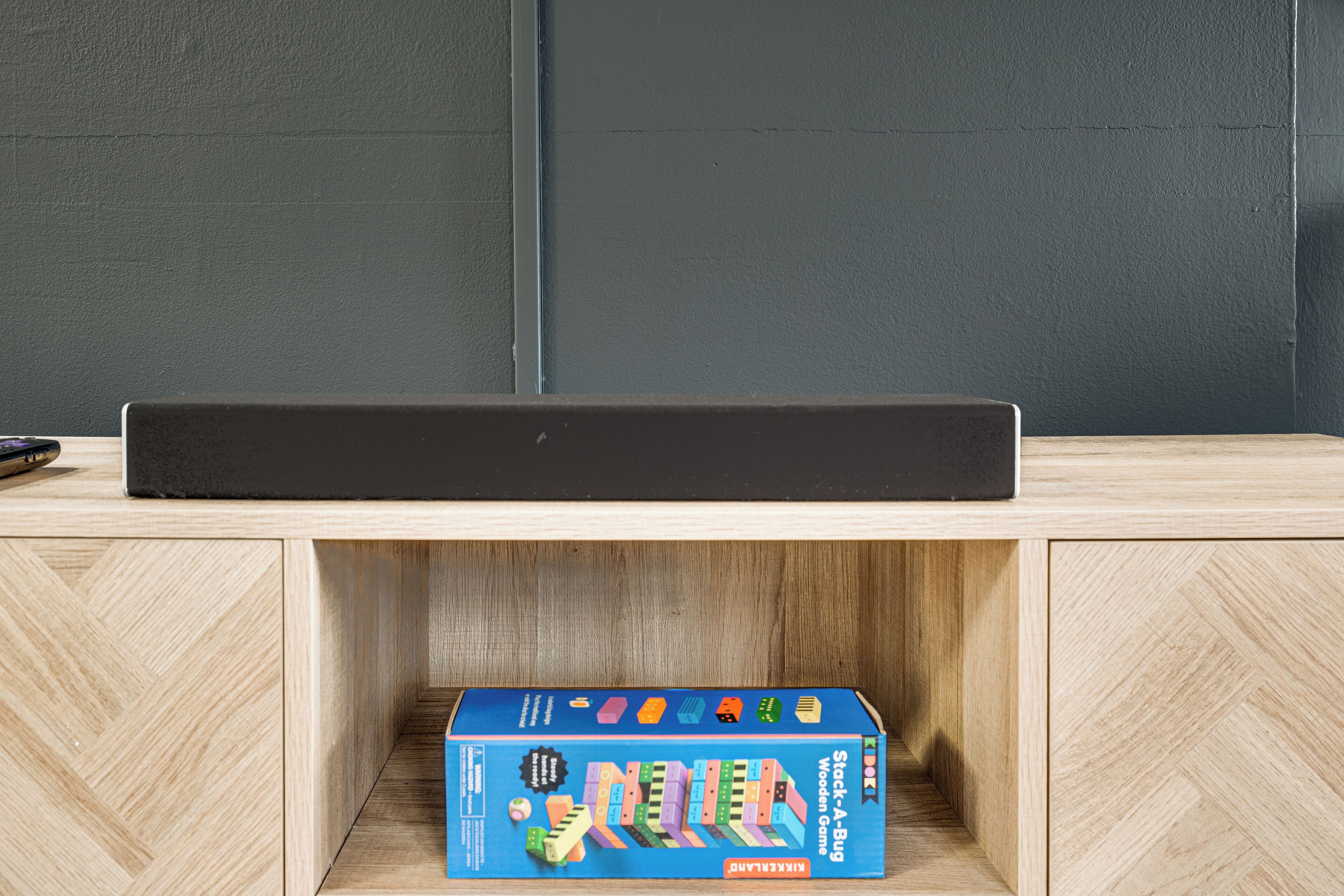 Un mueble de madera con una caja de juego de mesa azul etiquetada como “Stack-A-Bug Juegos de Madera” encima.