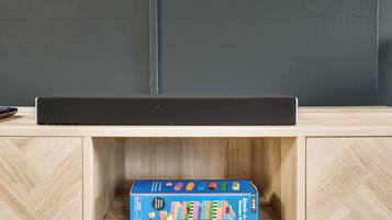 Un mueble de madera con una caja de juego de mesa azul etiquetada como “Stack-A-Bug Juegos de Madera” encima.
