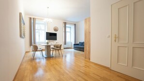 A spacious living area with a wooden floor, a dining table with chairs, a sofa, and a TV mounted on the wall. - Cozy 1BR apartment near Opera - 24h self check-in (Wien)