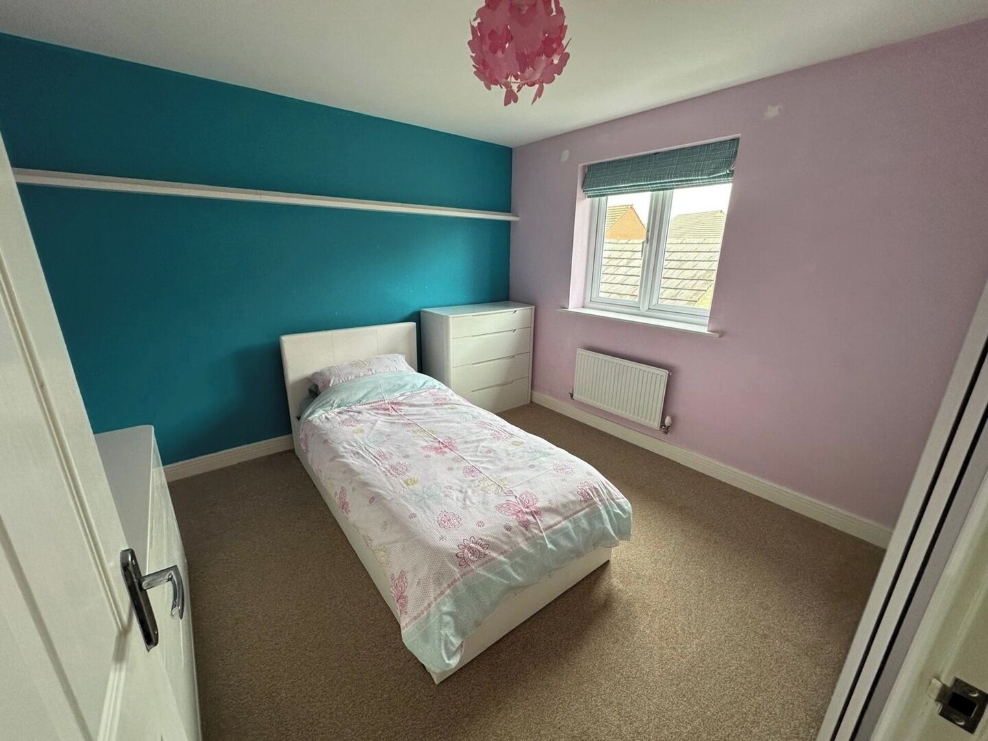 A bedroom with a bed, a dresser, a radiator, and a window with blinds.